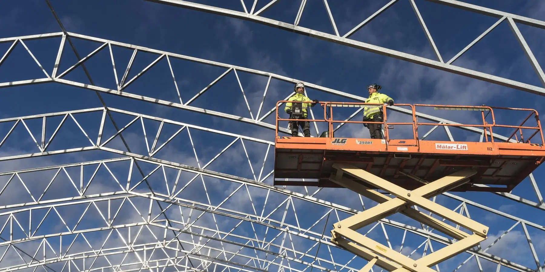 Dos técnicos sobre una plataforma de tijera bajo una estructura metálica